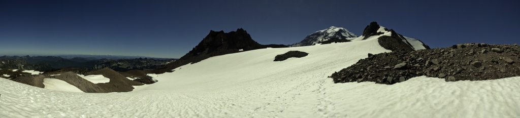 Panorama im Aufstieg zum Observation Rock (2549m), einem vulkanischen Felsen auf der Ostseite des Mt. Rainier (4359m); von Mowich Lake kommend über Spray Park erreichen wir auf mäßig steilen Firnfeldern den Sattel zwischen dem Echo Rock (2399m) auf der linken Seite und dem Observation Rock (2549m) auf der rechten Seite, während dazwischen der mehr als 1800m höhere Mt. Rainier (4359m) aufragt; am linken Horizont sind zwei weitere Vulkane auszumachen, bei denen es sich um den Mt. Baker (3285m) und den Glacier Peak (3213m) in den Northern Cascades handelt, Mt. Rainier NP, Washington