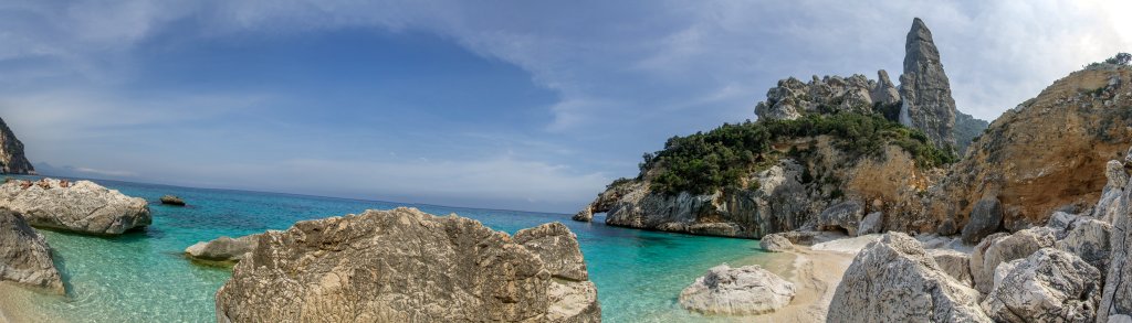 Türkisfarbenes Wasser am Strand der Cala Goloritze mit der sich darüber erhebenden Felsennadel der Punta Goloritze und einem interessanten Felsenbogen an der Küste, Sardinien, April 2014.