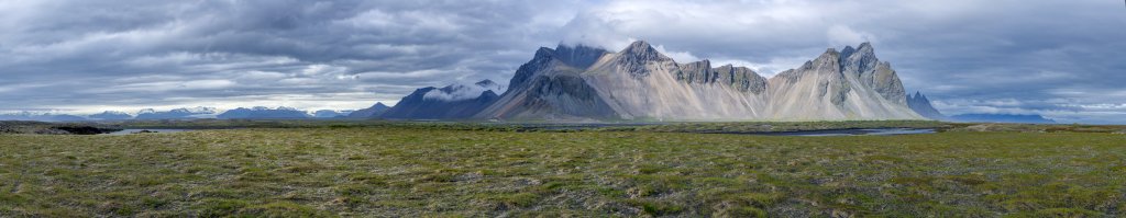 Blick vom Sandhaken Austurfjörur auf die Berggipfel der Halbinsel Stokksnes mit dem Fjardafjall (890m), dem Husadalstindur (674m), Kambhorn, Vestrahorn und Brunnhorn. In der Ferne hinter Höfn sind noch die östlichen Gletscherzungen des Vatnajökull zu erkennen, Island, Juli 2015.