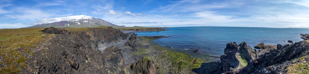 Blick auf die Steilküste und den schwarzen Sandstrand von Djupalonssandur über dem sich der von einer Fönwolkenwalze gekrönte Gipfel des Snæfellsjökull (1446m) erhebt, Island, Juli 2015.