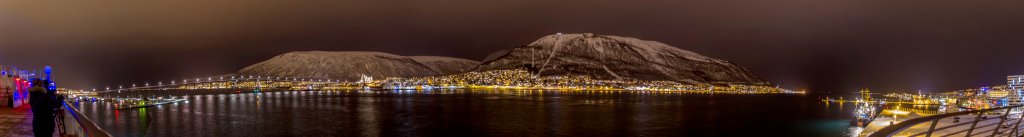 Bei Nacht im Hafen von Tromsø mit Blick auf die Hafenbrücke und die Eismeer-Kathedrale vor dem Bergrücken des Tromsdalstinden, Norwegen, Februar 2015.
