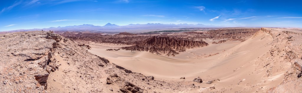 Blick vom nordwestlichen Rand des Valle de la Muerte auf die wild zerklüftete Felsenlandschaft und die großen Sanddünen des Tals. In Bildmitte erkennt man den Berg der Felsenfestung Quitor nahe des grünen San Pedro de Atacama und darüber den Vulkankegel des Licancabur (5920m), Chile, November 2016.