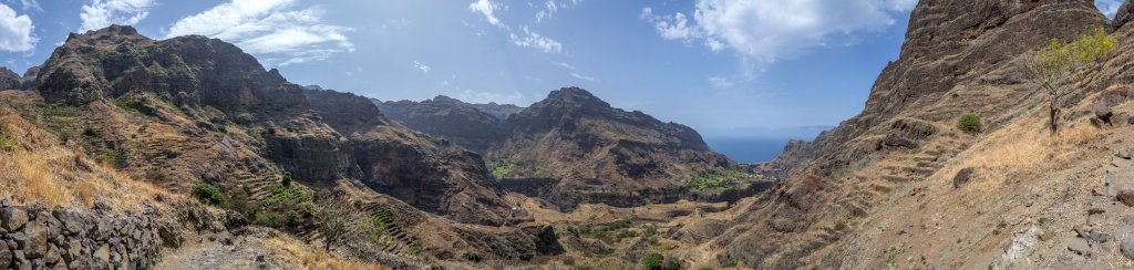 Auf alten Inselpfaden steigt man hinab ins tief eingeschnittene Tal Ribeira da Garca und schaut auf den auf einem grünen Plateau vor dem Meer gelegenen Ort Cha de Igreja, Kapverden, März 2016.