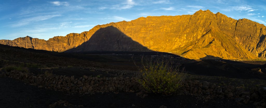 Beim Sonnenaufgang am Pico do Fogo (2829m) wirft der mächtige Vulkankegel seinen Schatten auf die im Sonnenlicht orange erglühende Ringmauer der Caldeira, Kapverden, März 2016.
