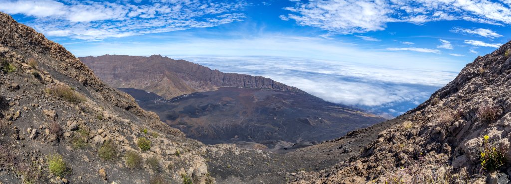 Vom Kraterrand auf 2779m Höhe blickt man hinunter auf den ca. 1000 Höhenmeter tiefer gelegenen weiten Boden der Caldeira des Pico do Fogo (2829m), die sich mit einem Lavaabfluss in östlicher Richtung zum Atlantischen Ozean hin öffnet, Kapverden, März 2016.