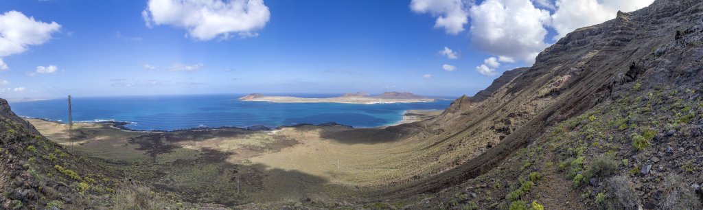 Abstieg auf dem Camino de Guatifay zum Playa del Risco unterhalb der steil aufragenden Felsencliffs des Risco de Famara und mit Blick auf die vorgelagerten Insel La Graciosa, Lanzarote, Kanarische Inseln, März 2017.