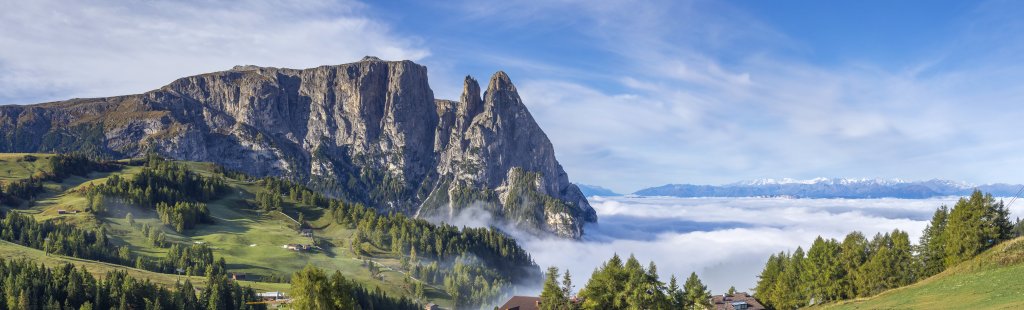 Frühmorgens an der Bergstation Compatsch (1851m) schweift der Blick über den Schlern (2568m), den Burgstall (2516m), die Punta Euringer (2394m), die Santnerspitze (2414m) über das im Morgennebel liegende Tal von Seis bis hinüber zur fernen Ortlergruppe, Seiseralm, Südtirol, Oktober 2019.