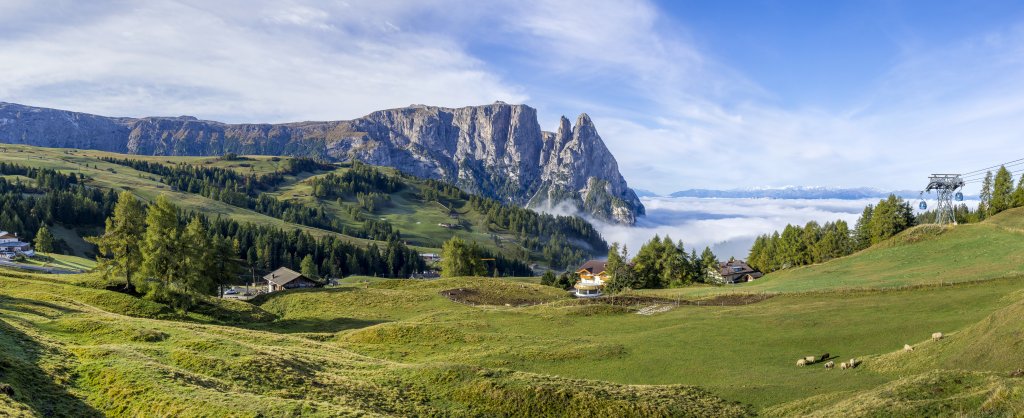 Frühmorgens an der Bergstation Compatsch (1851m) schweift der Blick über den Schlern (2568m), den Burgstall (2516m), die Punta Euringer (2394m), die Santnerspitze (2414m) über das im Morgennebel liegende Tal von Seis bis hinüber zur fernen Ortlergruppe, Seiseralm, Südtirol, Oktober 2019.