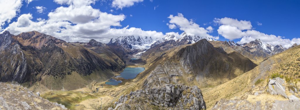 Ein letzter bereits wolkenumwölkter Panoramaausblick auf die nördliche Cordillera Huayhuash an einem felsigen Aussichtspunkt unterhalb des Cerro Huacrish (4750m), bevor ein steiler, grasiger Abstieg uns in das Tal der Quebrada Huacrish und zu unserem Zeltplatz (4086m) am Westufer der Laguna Jahuacocha führt, wo die aufgebauten Zelte unterhalb des Cerro Culebramina (5122m), des Cerro Berlin (5094m) und der Mina Punta (4780m) bereits zu sehen sind, Peru, Juli 2019.