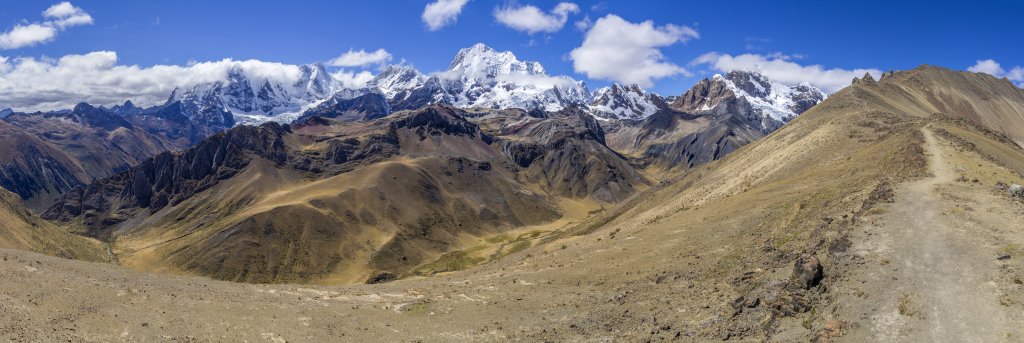 Großes Bergpanorama am Gratweg vom Pass Llaucha Punta (4838m) zum Gipfel des Cerro Huacrish (4750m) mit einem für wenige Minuten fast wolkenfreien Jirishance (6094m), Yerupaja Chico (6121m) und Yerupaja (6635m). Das felsige Vorgebirge über dem Tal der Quebrada Huacrish und Quebrada Tsacra ist von stark gefärbten Ascheschichten vulkanischen Ursprungs durchzogen, Peru, Juli 2019.