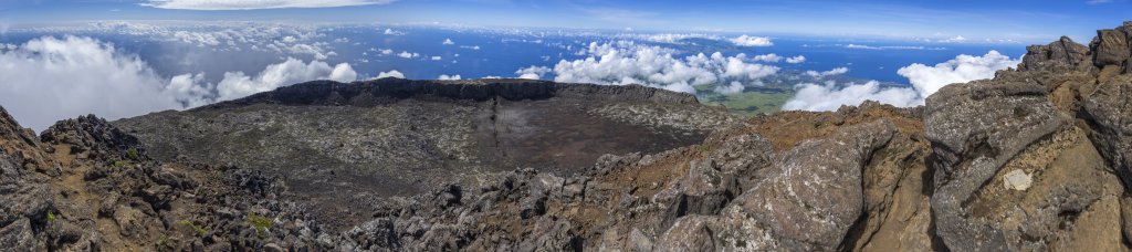 Tiefer Blick vom zentralen Vulkanspitz des Montanha do Pico (2351m) in die umgebende Ringcaldera, durch die ein beeindruckender radialer Riß verläuft. Gegenüber liegt die bis zu 1043m hohe Nachbarinsel Faial mit ihrem Haupthafen Horta, Pico, Azoren, Portugal, September 2022.