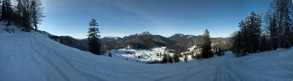 Panorama im Abstieg vom Schildenstein (1613m) über die Königsalm (1115m). Zu sehen ist die Benediktenwand, der Schönberg, Ross- und Buchstein, der Hirschberg und der Leonhardstein. Unten im Tal liegen die Weideflächen der Königsalm. Mangfallgebirge, Januar 2010.