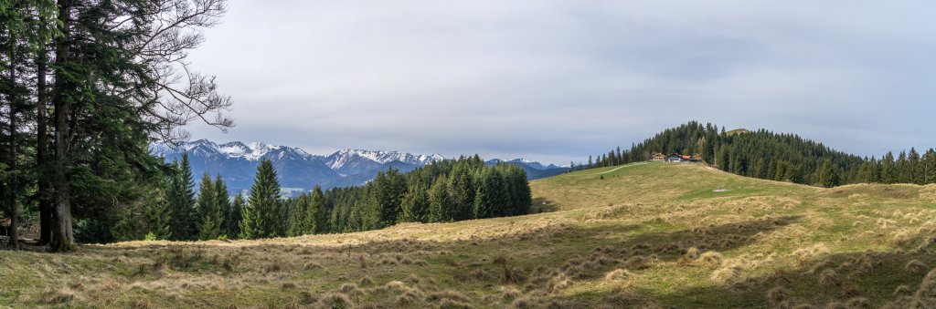 Die Schwarzenberg-Alm vor dem Gipfel des Schwarzenbergs (1187m) und mit den noch verschneiten Gipfeln des Rotwand- und Spitzinggebiets im Hintergrund, darunter die markante Brecherspitze, Mangfallgebirge, Bayrische Alpen, April 2016.