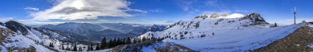 Großes winterliches Gipfelpanorama am Rotwandhaus (1737m) im Spitzinggebiet unterhalb der von der Sonne angestrahlten Rotwand (1884m) und vis-a-vis dem Hinteren Sonnenwendjoch (1986m), Mangfallgebirge, Dezember 2018.