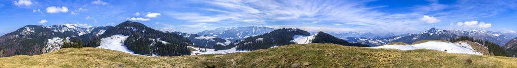 360-Grad-Panorama am Gipfel eines namenlosen, grasigen Kofels oberhalb der Rettenbachalm (1202m) bei Sachrang mit weitem Rundumblick auf Mühlhörndl, Mühlhornwand und Geigelstein (1808m), den Wandberg, den langgestreckten Rücken des Brennkopfes, Wilden und Zahmen Kaiser, Karspitze, auf die Berge des Sudelfelds mit Brünnstein und dem Trainsjoch sowie Spitzstein, Tristmahlnschneid, Zinnenberg und Klausenberg, Südliche Chiemgauer Alpen, Österreich, April 2019.
