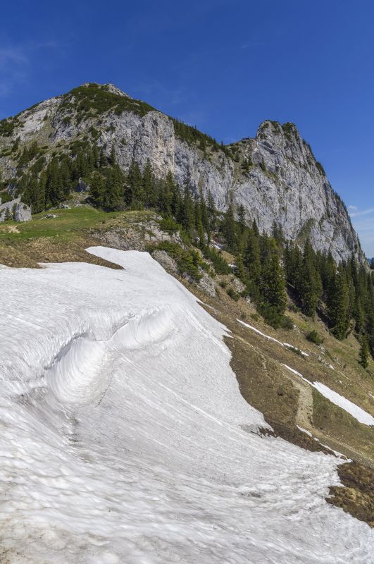 Vertikalpanorama - Beeindruckende Wächte am Übergang vom Sonnberg zu den Rosssteinalmen mit Blick auf den Rossstein (1698m), die Tegernseer Hütte (1650m) und den Buchstein (1701m), Mangfallgebirge, Bayrische Alpen, Juni 2019.